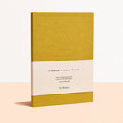 A notebook with a mustard yellow textured cover, a white paper band across the middle, and a matching yellow lower section. The front text reads 'A Notebook for Ordinary Moments' and shows the brand 'The Blindry'.